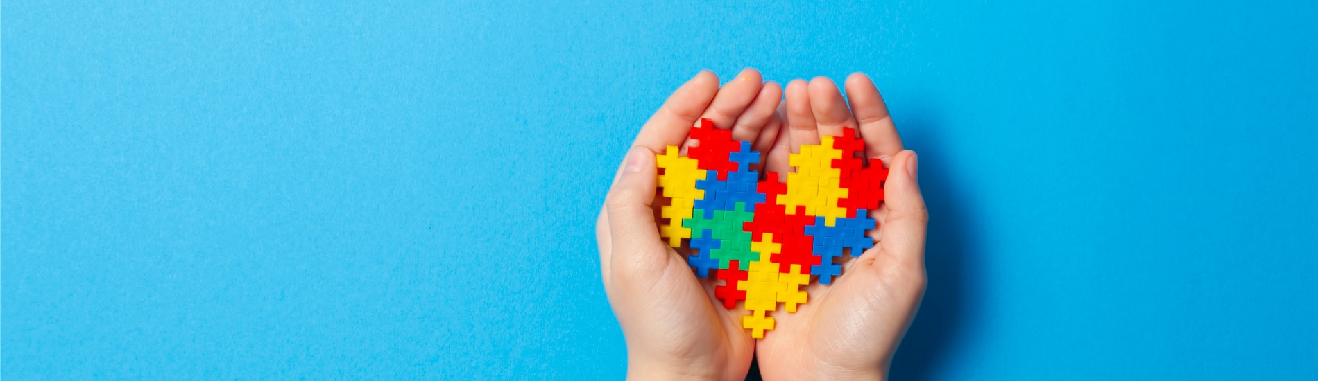 In zwei geöffneten Händen liegt ein Herz aus bunten Plastikpuzzle-Steinen.